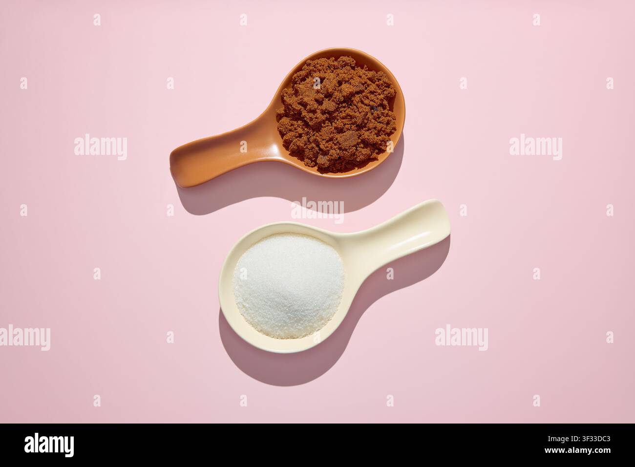 Muscovado-Zucker und weißer granulierter Zucker nebeneinander auf rosa Hintergrund Stockfoto