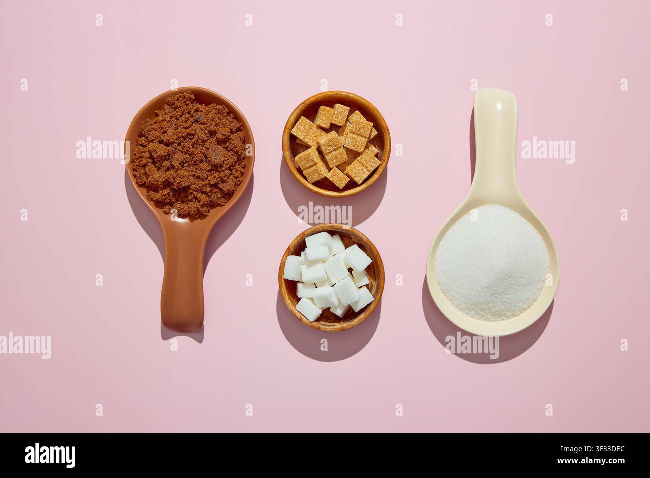 Sortiment aus Zucker auf rosa Hintergrund. Muscovado, weißer Kristallzucker, weiße Zuckerwürfel und braune Zuckerwürfel. Stockfoto