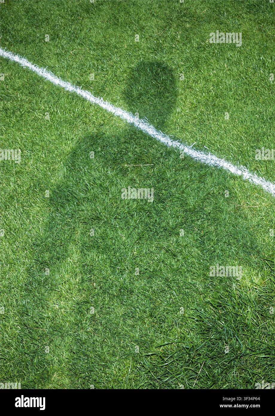 Schatten einer stehenden Person, der auf ein grünes Sportfeld mit weißer Markierung geworfen wird Stockfoto