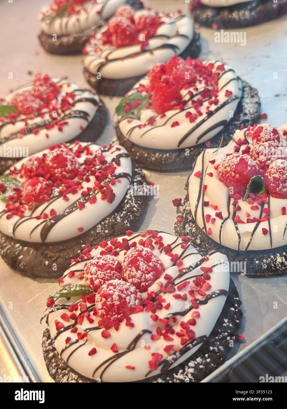 Schokoladenkekse mit weißer Sahne, frischen Himbeeren und Schokoladensoße in einer Bäckerei ausgestellt. - Smartphone-aufgenommenes Stockfoto