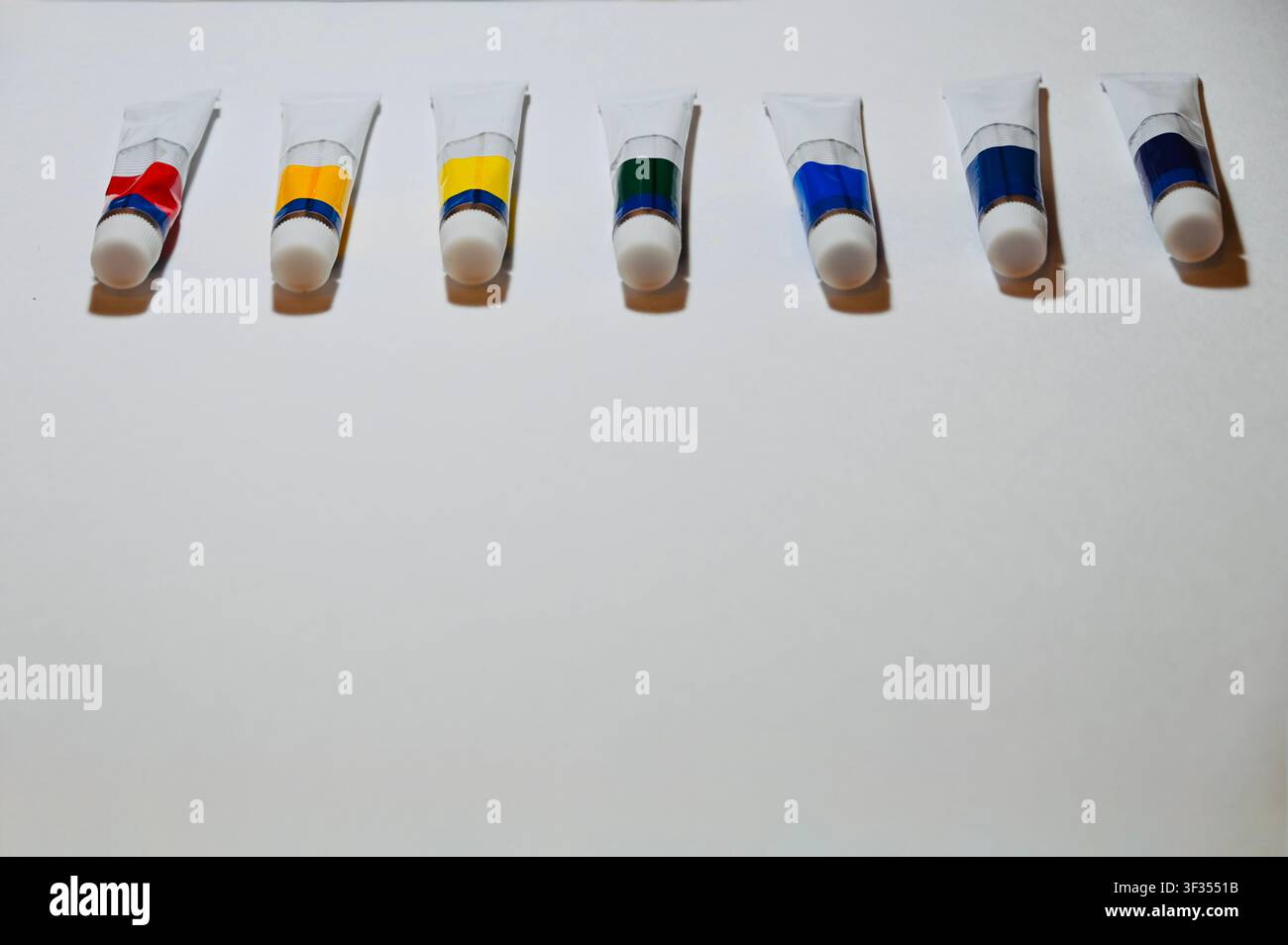 Reihe von Farbe Vertikale Hochwinkelaufnahme von bunten Acryl- oder Ölfarbtuben, die ordentlich in einer Reihe auf einem weißen Hintergrund angeordnet sind, mit Platz für Text. Minimalistischer Hintergrund ideal für Kunststudio, Malerei, Kunstbedarfskatalog, Design und pädagogische Konzepte. auf weißer Oberfläche mit Kopierraum. Hochwertiges Foto Stockfoto