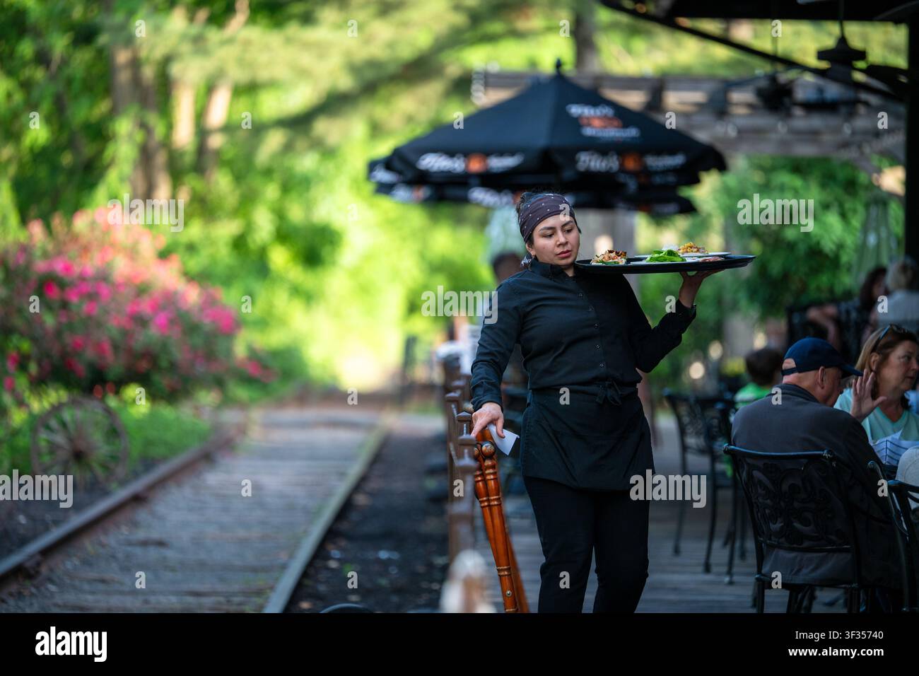Restaurantkellner trägt ein Tablett mit Essen zu Gästen im Freien in Lambertville, New Jersey, USA, an einem geschäftigen Sommerabend. Stockfoto
