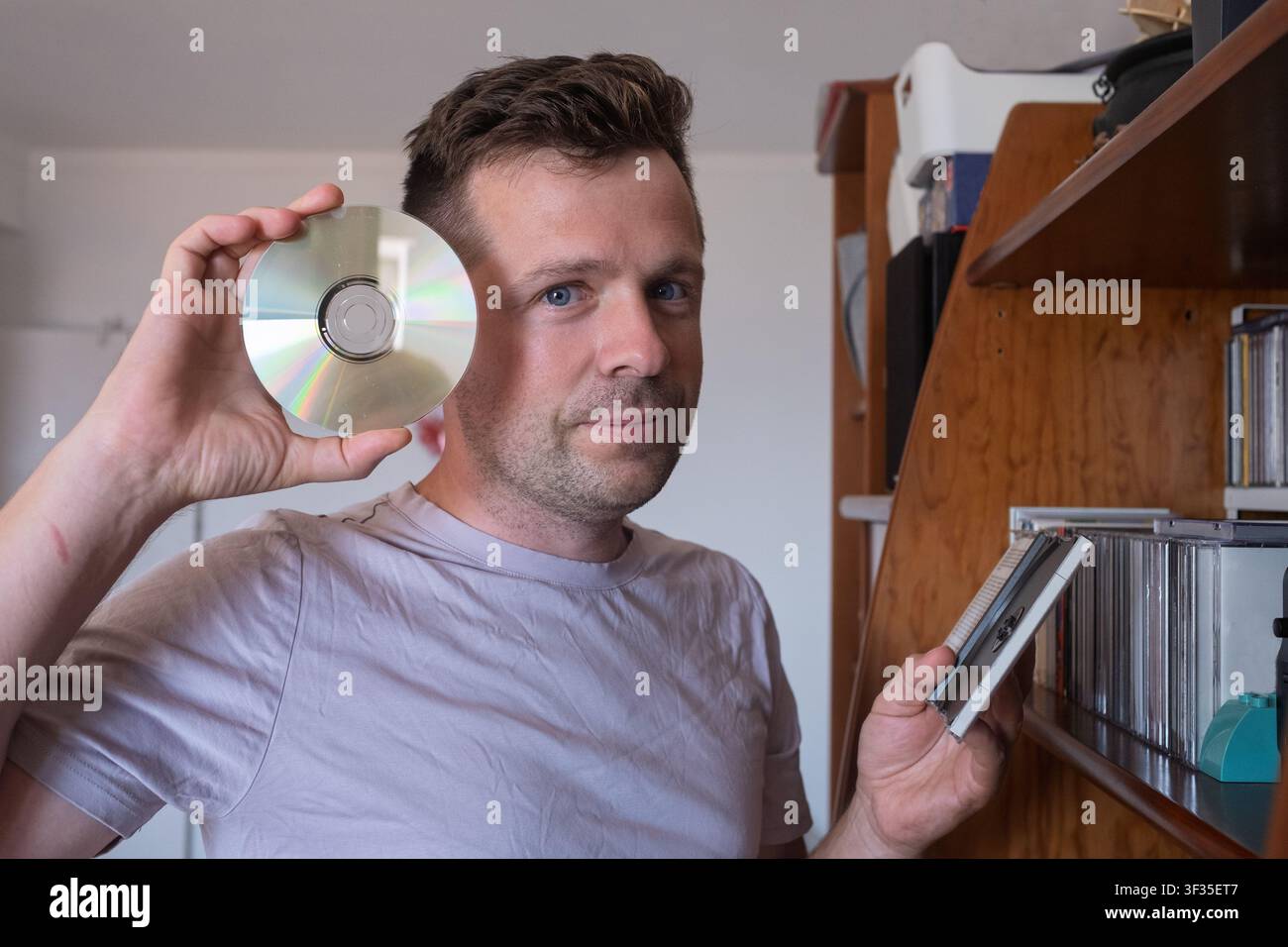 Mann hält eine Compact Disc in der Nähe eines Bücherregals. Stockfoto