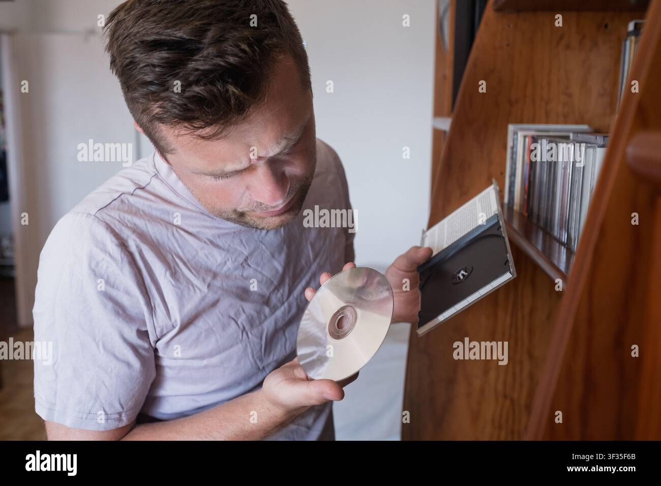 Mann hält eine Compact Disc in der Nähe eines Bücherregals. Stockfoto