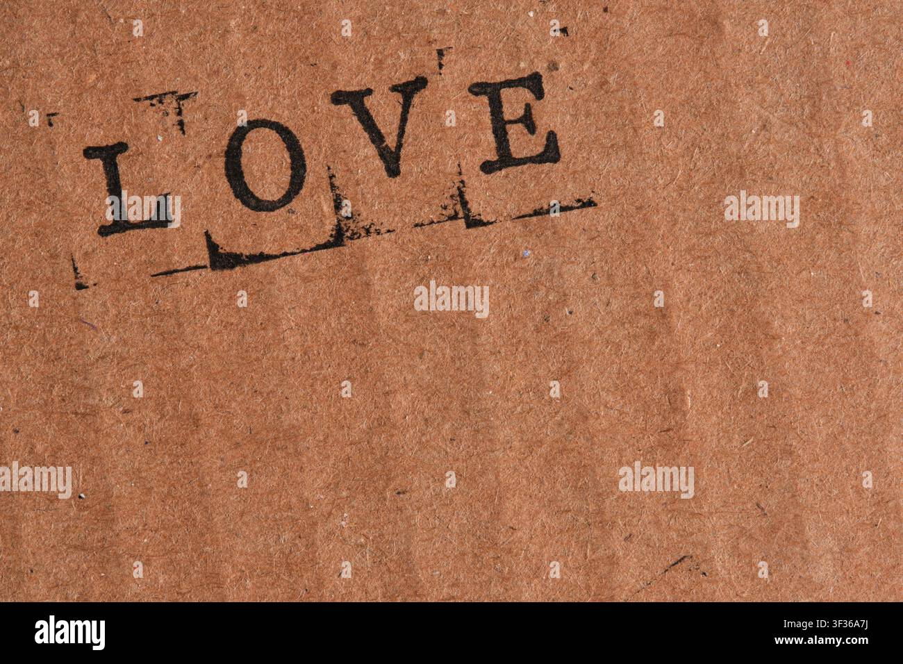 Das Wort LIEBE in dunkler schwarzer Tinte in der oberen Ecke auf braunem Kartonhintergrund gestempelt Stockfoto