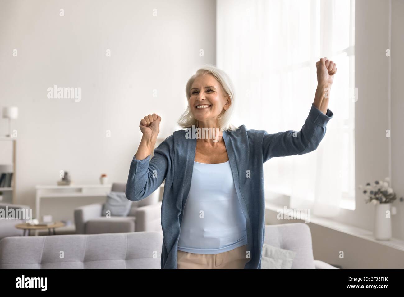 Aktive, freudige ältere Frau, die allein im Wohnzimmer tanzt Stockfoto