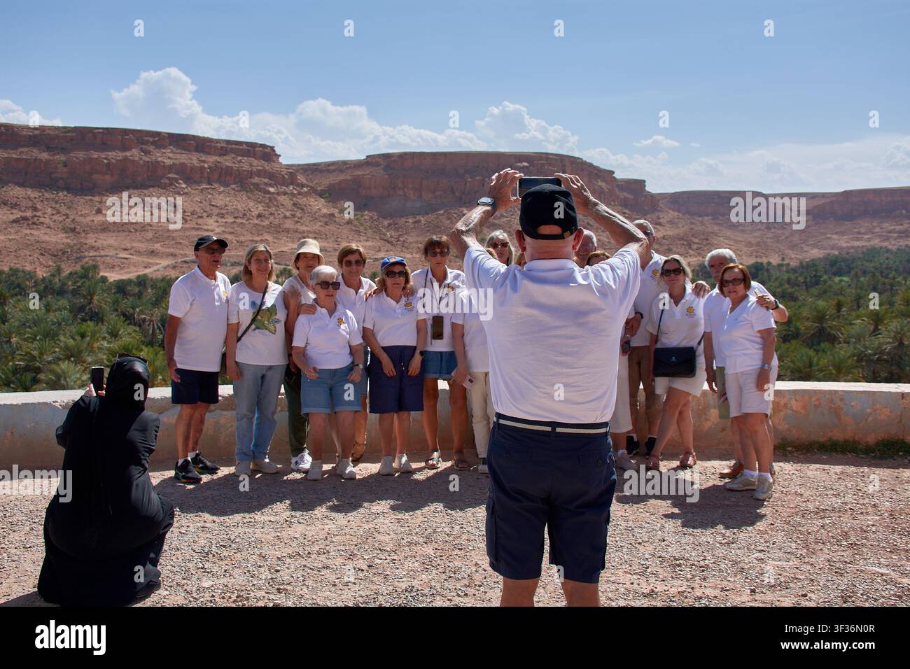 Tafilalet-Palmenhain, Marokko, 30. Mai 2026, Eine große Gruppe von Seniorentouristen in weißen T-Shirts posiert fröhlich, während ein Kollege ihr Foto macht Stockfoto