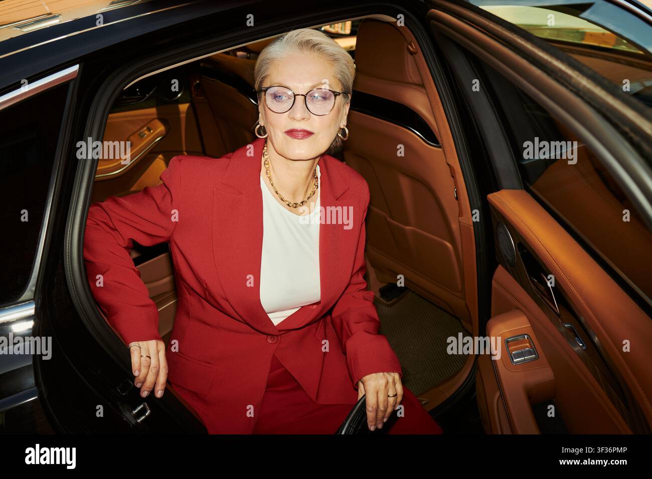 Kaukasische Senior-Businessfrau sitzt in einem Luxusauto, bereitet sich auf die Ankunft bei einer Firmenveranstaltung vor, vermittelt Führungserfolg und Premium-Lebensstil. Nützlich für Führungskräfte-Branding und Luxus-Marketing Stockfoto