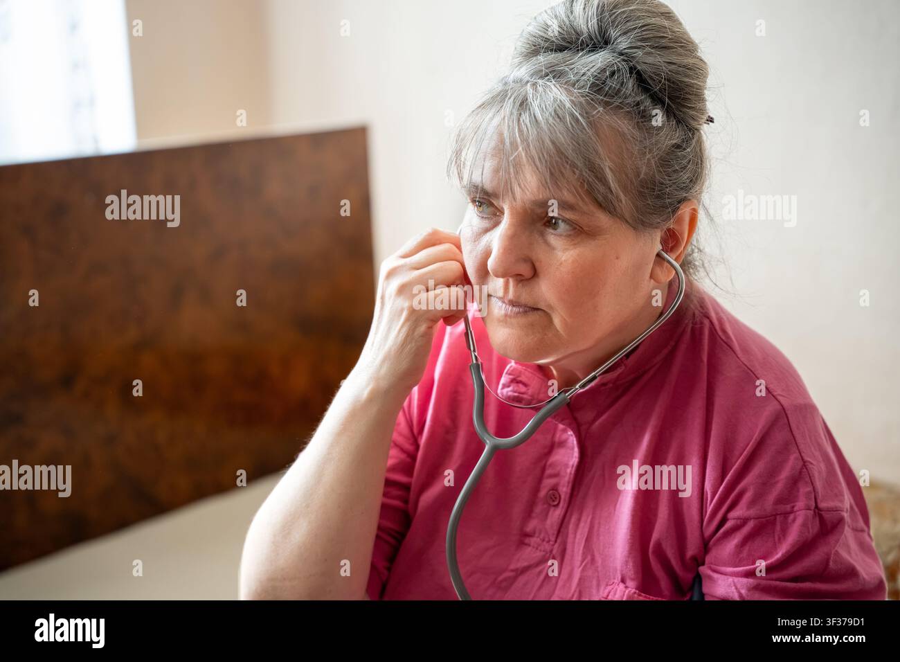 Seniorin verwendet Stethoskop zur Überwachung der Herzgesundheit zu Hause. Selbstfürsorge für die Herz-Kreislauf-Gesundheit und Bewusstsein für die Menopause. Stockfoto
