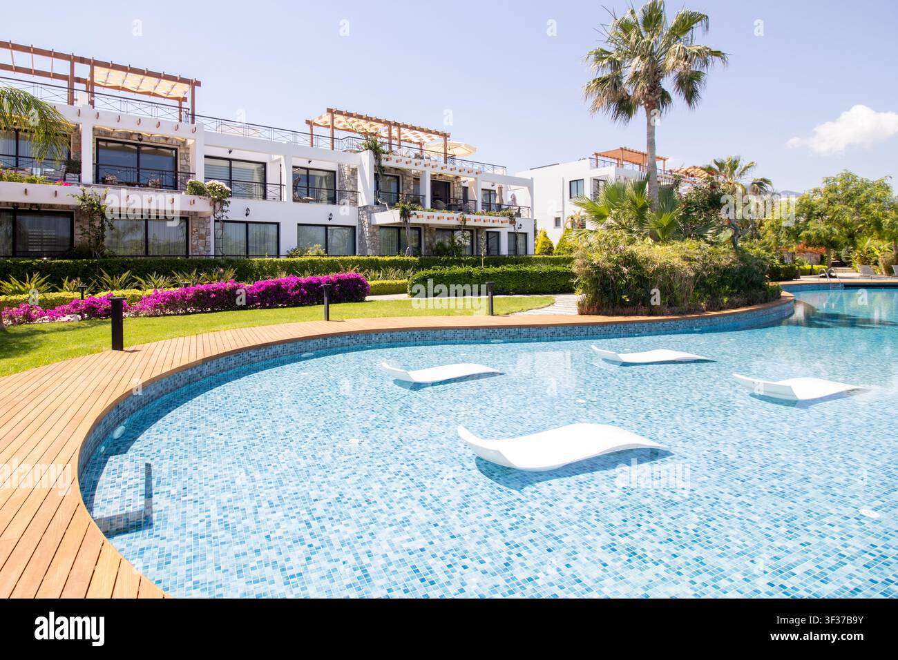 Luxus-Ferienwohnungen mit einem geschwungenen Schwimmbecken, das über im Wasser liegende Loungesessel verfügt, in einer landschaftlich gestalteten Resort-Umgebung an einem sonnigen Tag Stockfoto