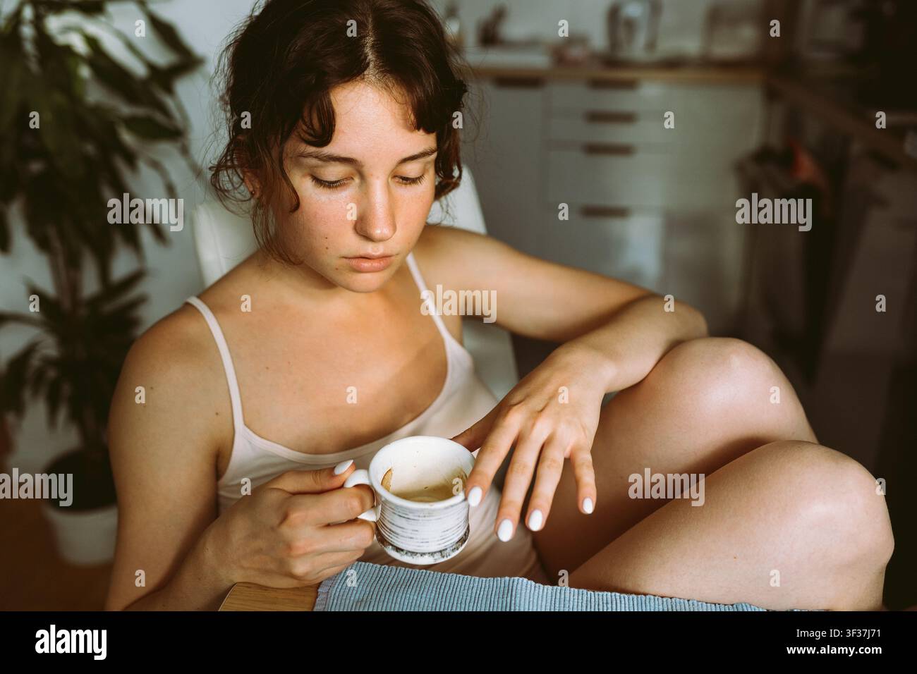 Junge Frau, versunken in Gedanken, mit Morgenkaffee in der Küche Stockfoto