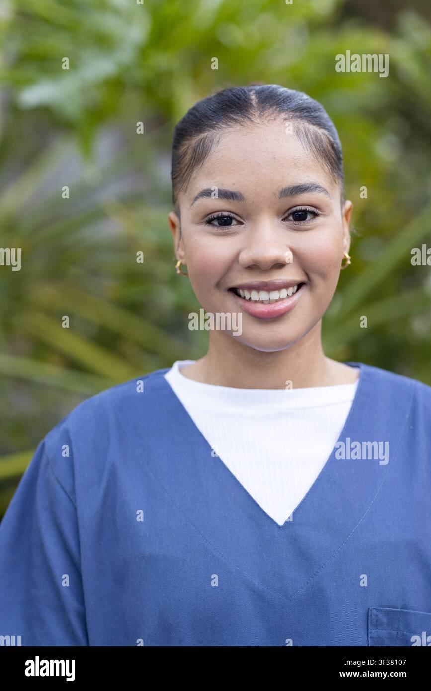 Krankenschwester in blauen Kitteln und weißem geripptem Unterhemd lächelt, posiert im Garten mit goldenen Reifen Stockfoto