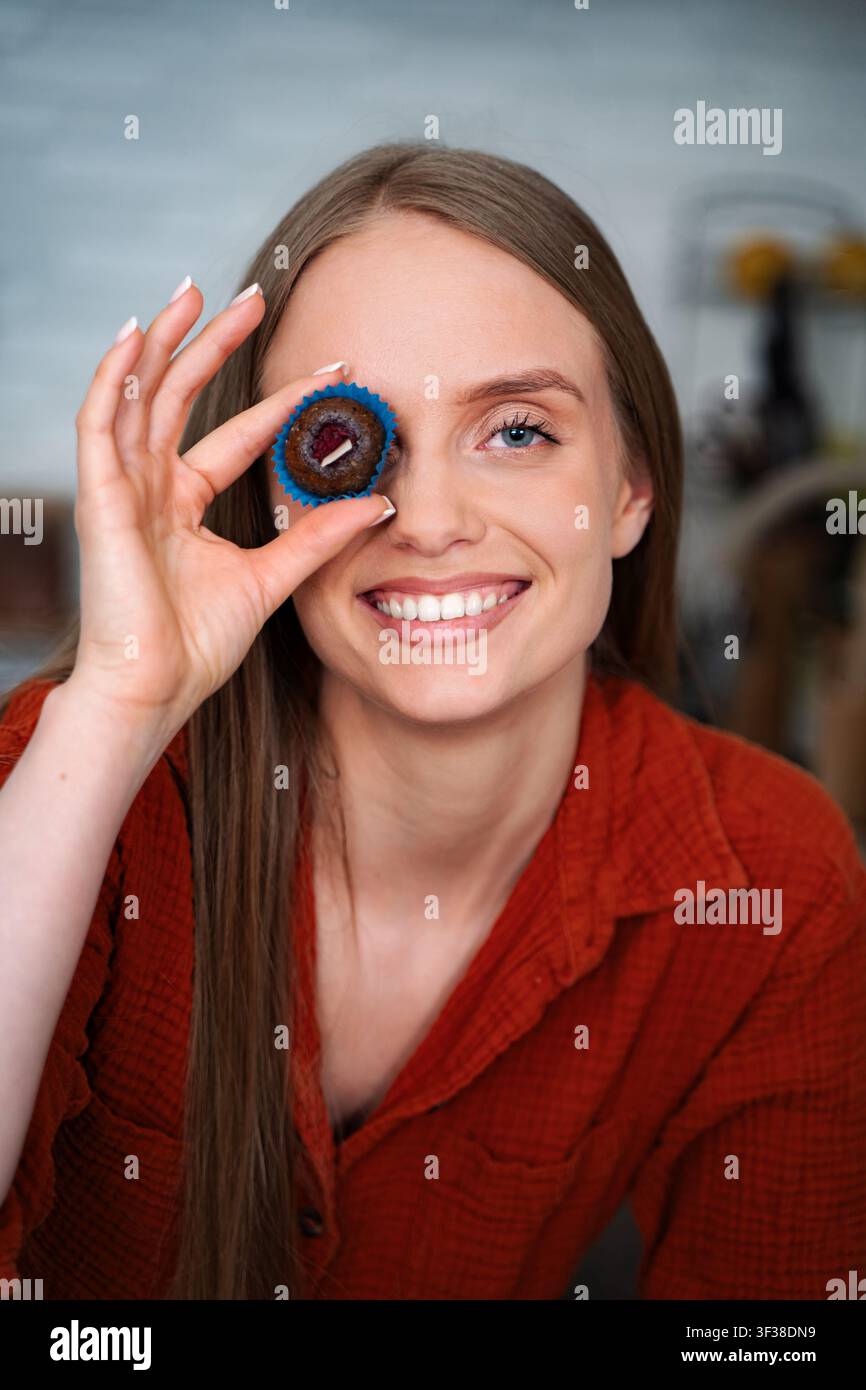 Eine junge Frau lächelt und hält einen Cupcake über dem Auge Stockfoto