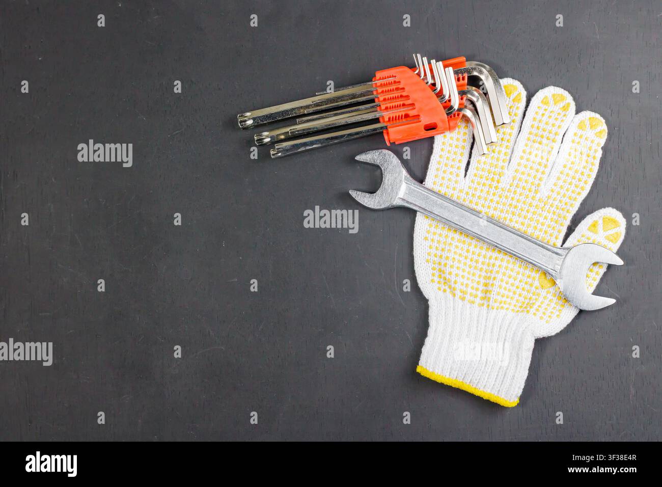 Ein Satz Sechskantschlüssel, ein Metallschlüssel und ein weißer Arbeitshandschuh, die auf einer dunklen Oberfläche angeordnet sind, mit Kopierraum links. Hochwertiges Foto Stockfoto
