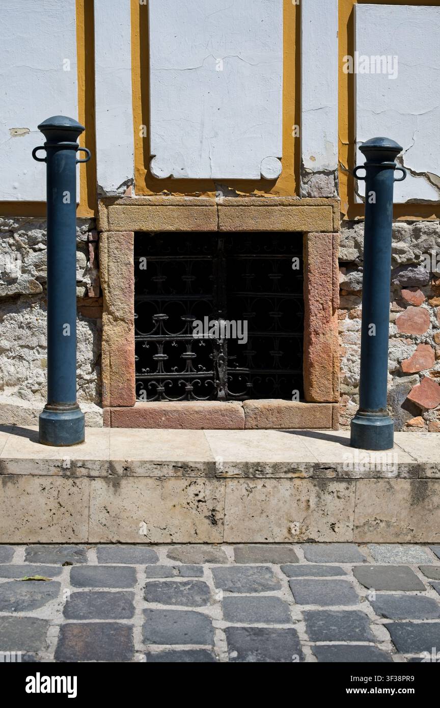 Architektonisches Detail eines historischen Steingebäudes mit Kellerschlusslicht, schmiedeeisernem Gitter und Metallpflockern in Szentendre, Ungarn. Stockfoto