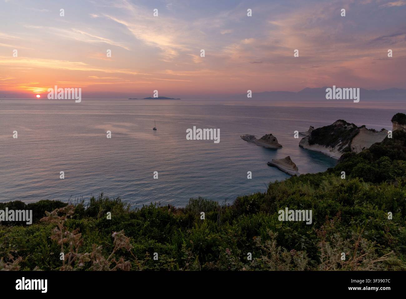 Sonnenuntergang zur goldenen Stunde über dem ruhigen Ionischen Meer, der einzigartige Felsformationen und ein fernes Segelboot hervorhebt Stockfoto