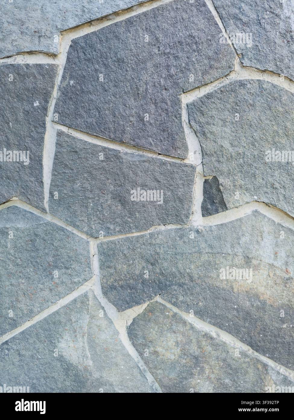 Nahaufnahme einer modernen grauen Schieferplattenwand mit sauberen weißen Mörtelfugen und unregelmäßigen geometrischen Formen. - Smartphone-aufgenommenes Stockfoto
