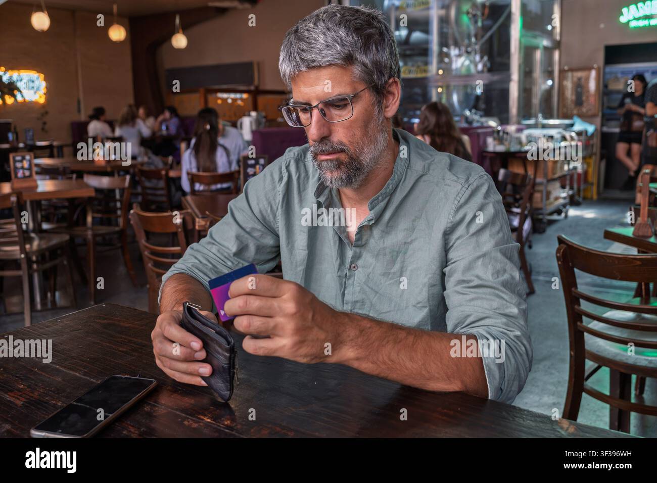 Reifer Mann, der eine Brieftasche und eine Kreditkarte an einem Cafétisch hält, eine gängige Szene moderner finanzieller Transaktionen und Lebensstils Stockfoto