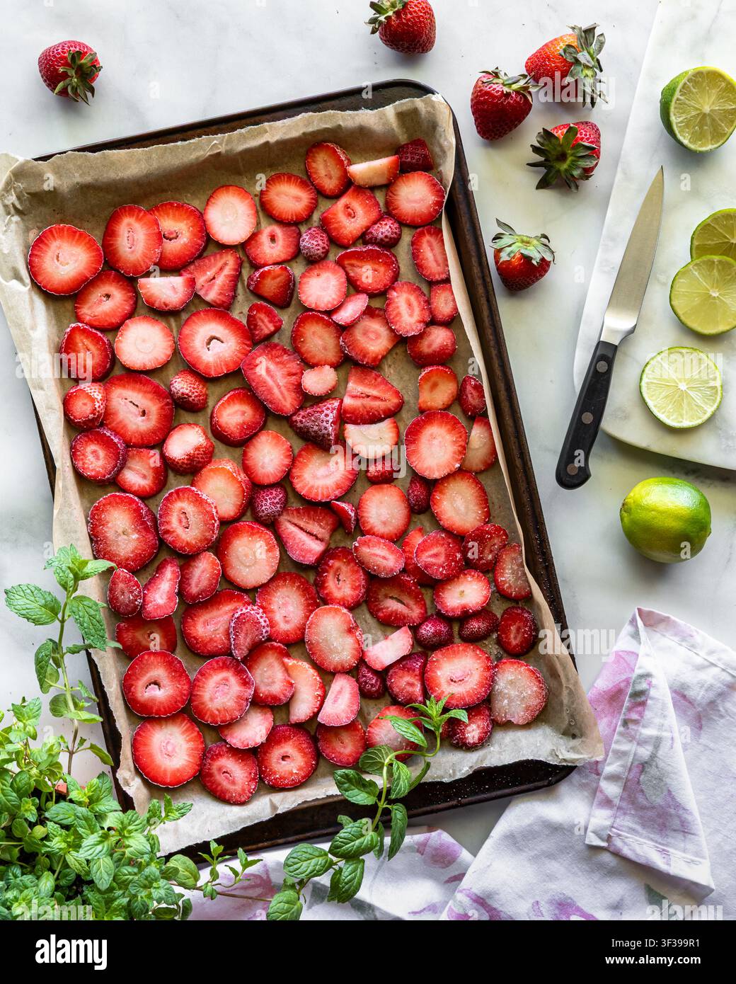 Ein pergament ausgelegtes Backblech mit gefrorenen Erdbeerscheiben zum Schnellgefrieren. Stockfoto