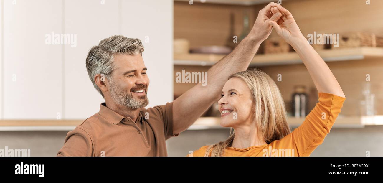 Fröhliches Paar tanzt in der Küche, lächelt zusammen, freudiger Moment Stockfoto