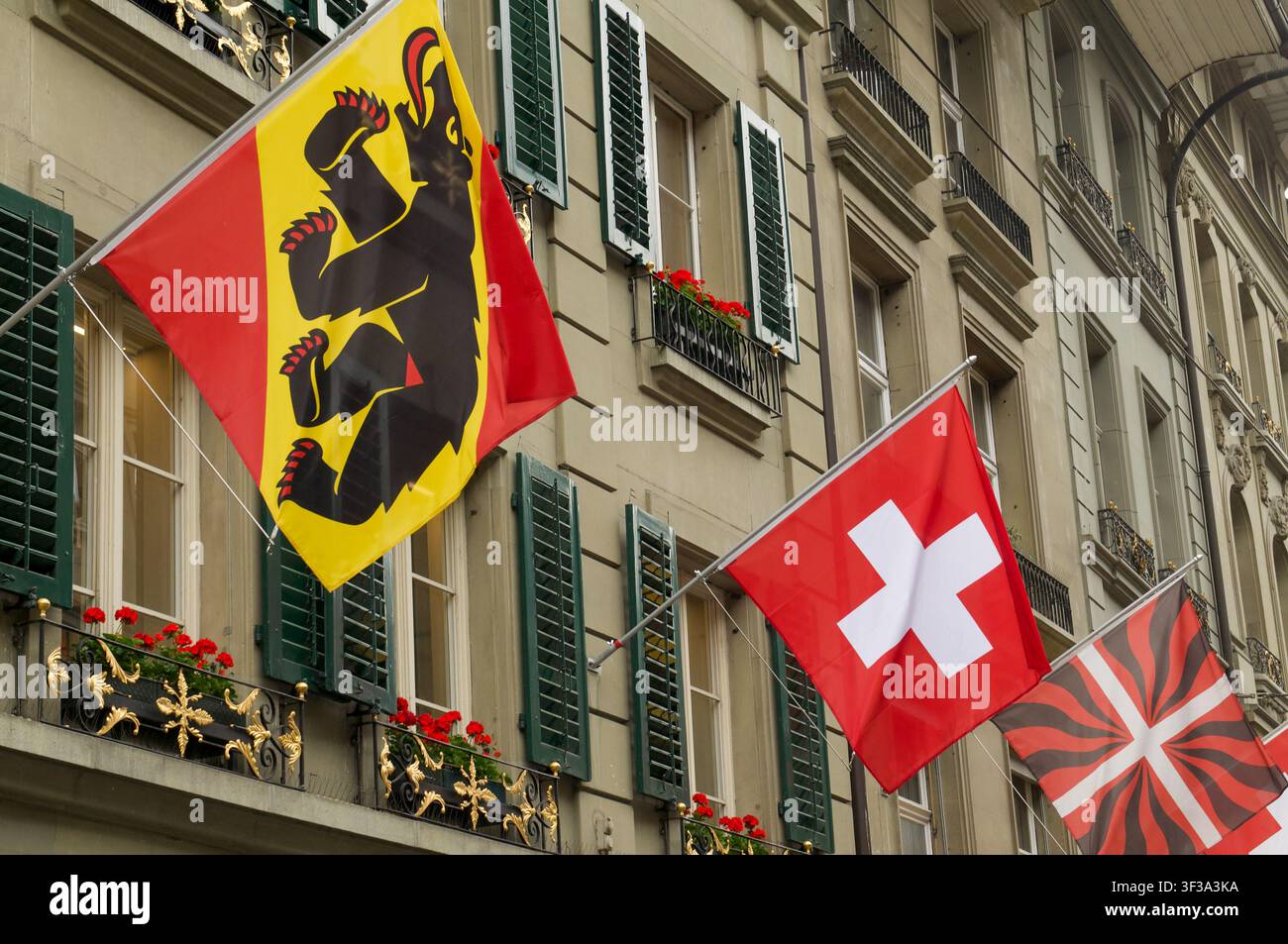 Reihe traditioneller Flaggen, die an einer historischen Gebäudefassade in Bern wehen. Blick auf die Bärenflagge des Kantons Bern, die Schweizer Nationalkreuzflagge und die t Stockfoto