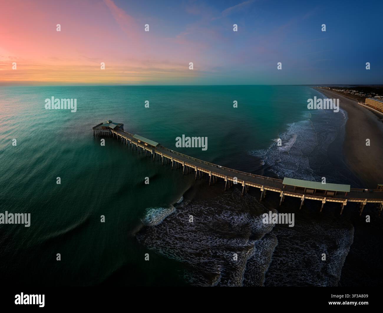 Folly Beach, South Carolina, in den ruhigen Momenten vor der Morgendämmerung. Der Horizont leuchtet in Orange und Rosa und geht über in einen ruhigen blauen Himmel, der mit f Stockfoto