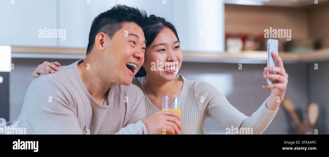 Fröhliches asiatisches Paar macht zusammen in der Küche ein Selfie, lächelt und genießt den Moment Stockfoto