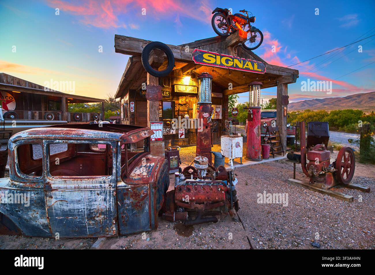 Verlassene antike Tankstelle mit verrostetem Auto und Vintage-Pumpen zur Goldenen Stunde Stockfoto