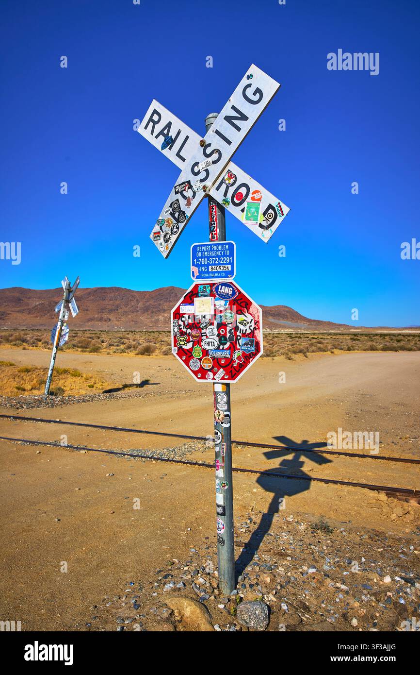 Bahnübergangs-Schild mit Aufklebern und Bahngleis in der Wüstenlandschaft Kaliforniens Stockfoto