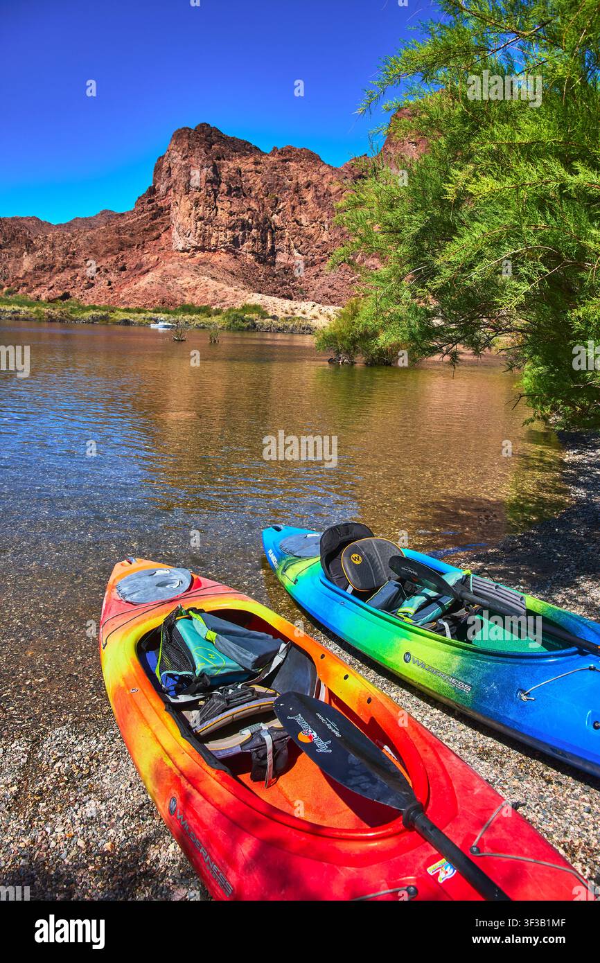 Bunte Kajaks an einem Kiesufer am Colorado-Fluss mit Wüstenklippen und grünem Laub Stockfoto