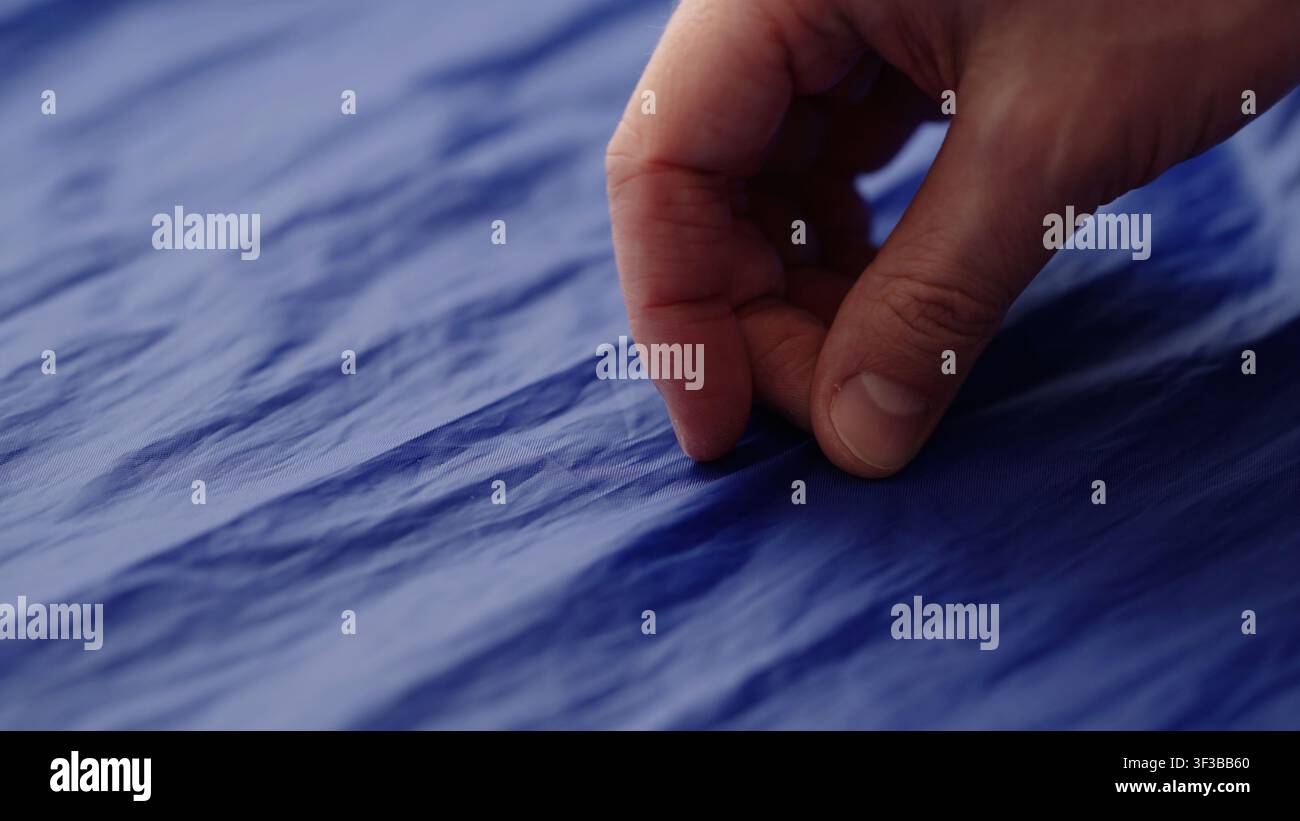 Männerhand prüft blauen Kunststofftaschenstoff Stockfoto