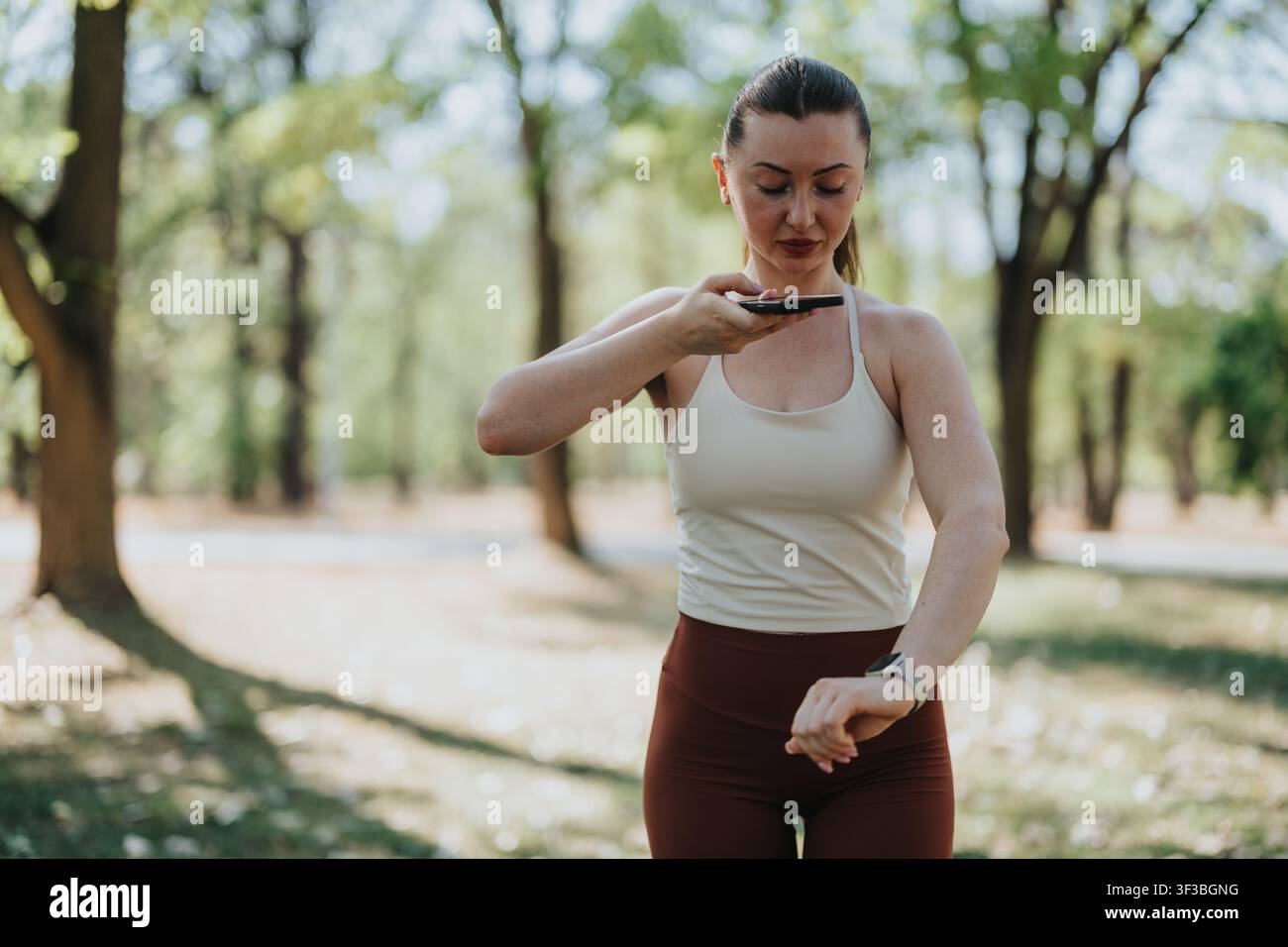 Fitnessfrau verwendet Smartphone und Smartwatch während eines Outdoor-Fitness-Workouts im Park Stockfoto