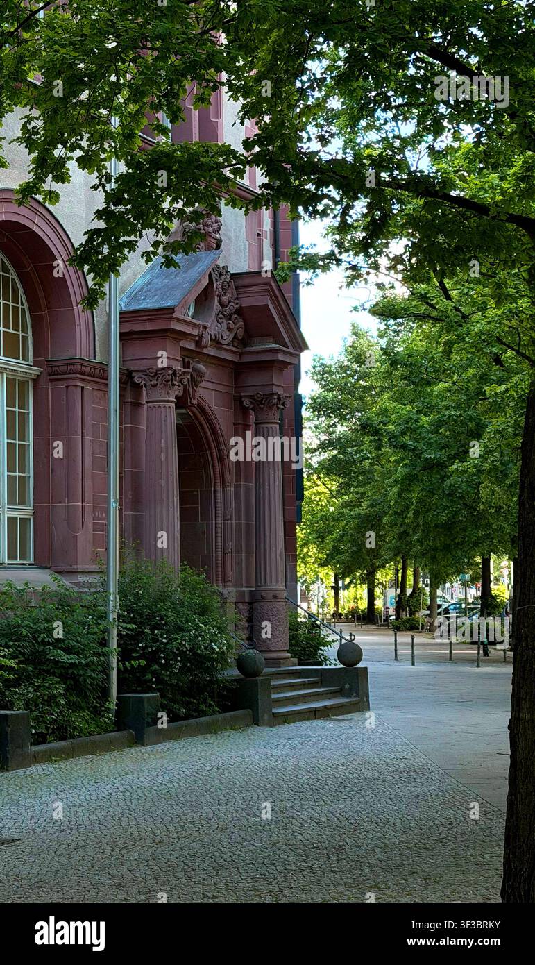 Eckgebäude mit historischer, verzierter Architektur und üppiger Vegetation entlang eines Kopfsteinpflasterweges, Berlin Stockfoto