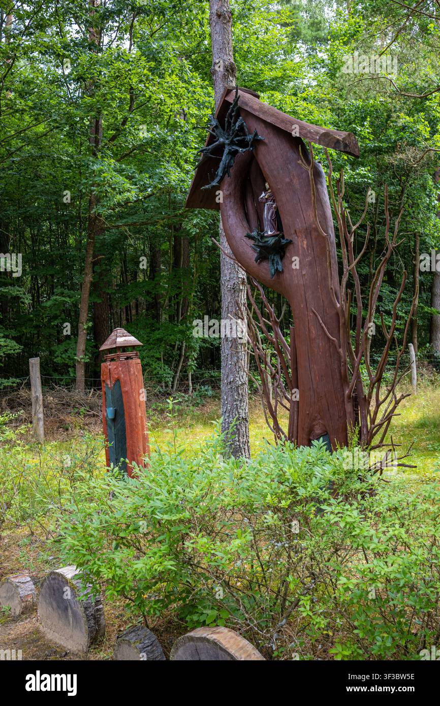 Handgefertigte Holz-Kunstinstallation mit einer Figur von Jesus, umgeben von hohen Bäumen, in einem ruhigen Waldskulpturengarten Stockfoto