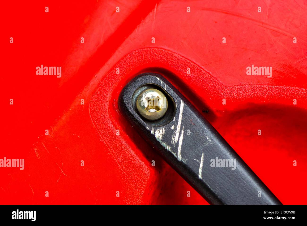 Ein schwarzes Plastikband mit Metallschraubverschluss, das an einer zerkratzten roten Plastikoberfläche befestigt ist, Nahaufnahme, die Textur und Abnutzung zeigt Stockfoto
