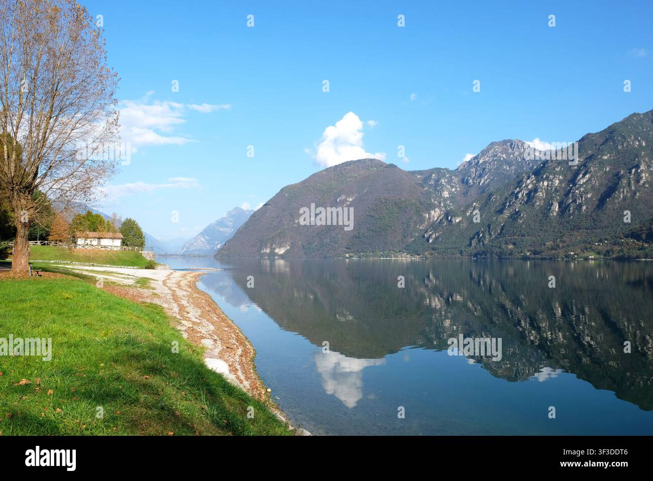 Der malerische Idrosee in den italienischen Alpen mit klarem Wasser, das die umliegenden Berge an einem sonnigen Tag widerspiegelt. Stockfoto