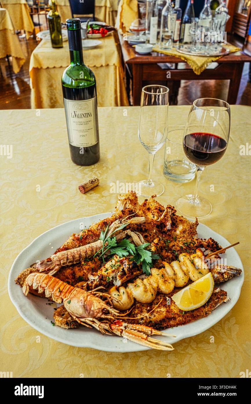 Gegrilltes Meeresfrüchte-Platte mit Garnelen und Fisch, serviert mit Zitrone und einer Flasche Rotwein in einem Restaurant. Abruzzen, Italien, Europa Stockfoto