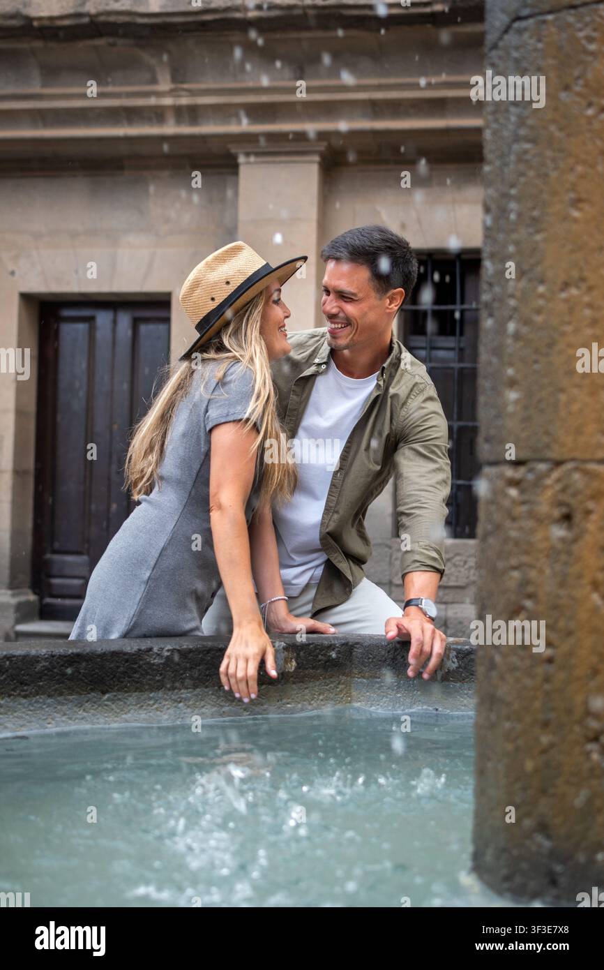 Glückliches Paar genießt einen verspielten Moment an einem historischen Brunnen, während es die Altstadt erkundet. Stockfoto