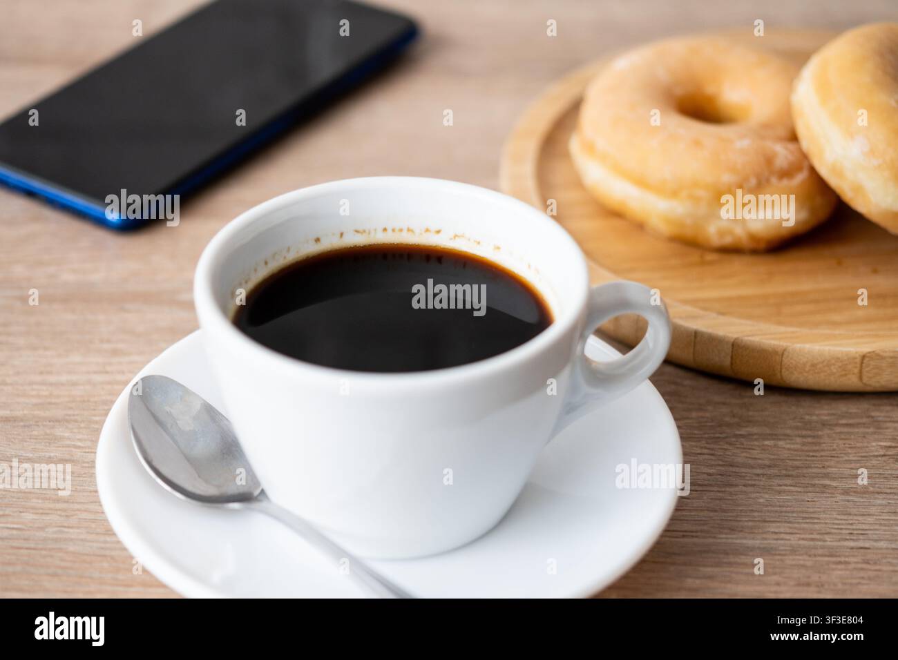Schwarzer Kaffee mit glasierten Donuts und Smartphone auf Holztablett Stockfoto