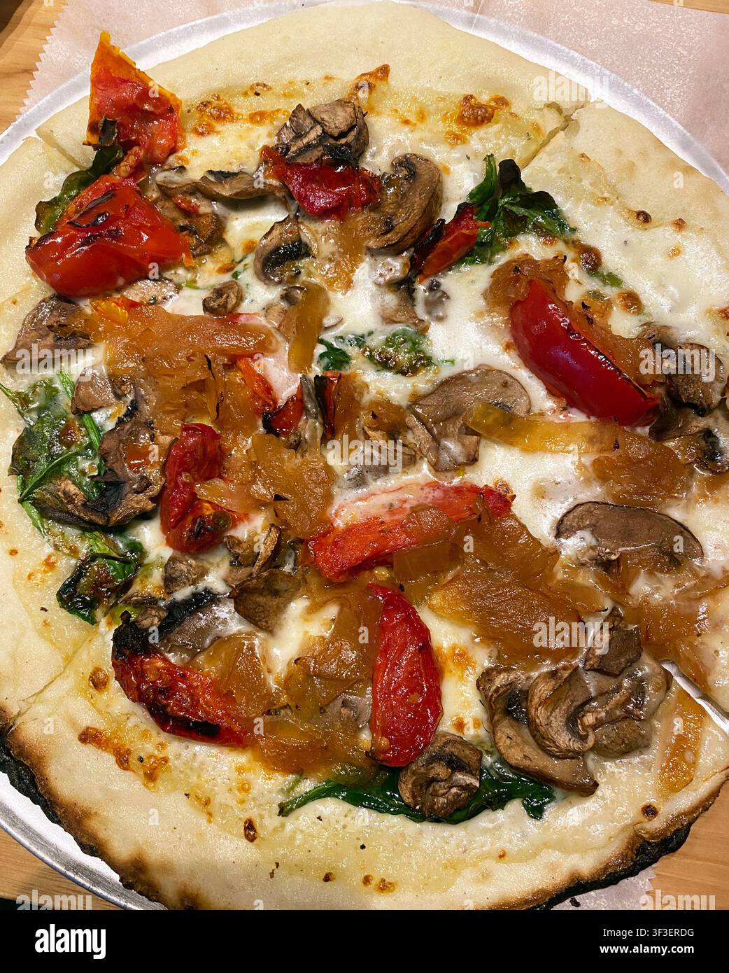 Eine Nahaufnahme einer Pizzascheibe mit roten Paprika, Pilzen, Spinat, Zwiebel und weißem Käse, keine rote Soße-Pizza. - Smartphone-aufgenommenes Stockfoto