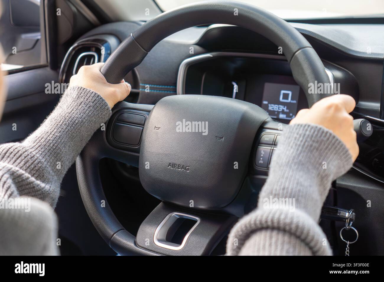 Detail der Hände eines Fahranfängers, die das Lenkrad umklammern, digitaler Geschwindigkeitsmesser zeigt null, Airbag-Aufkleber, Autoinnenraum, Konzept des Fahrlernens Stockfoto