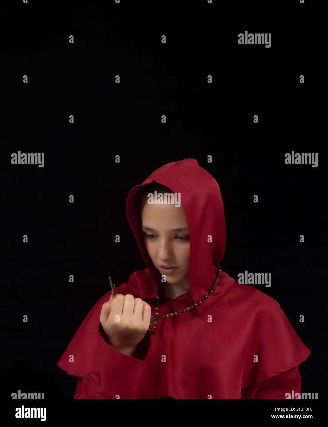 Geheimnisvolle Frau in rotem Kapuzenmantel posiert in dunklem dramatischem Studio Stockfoto