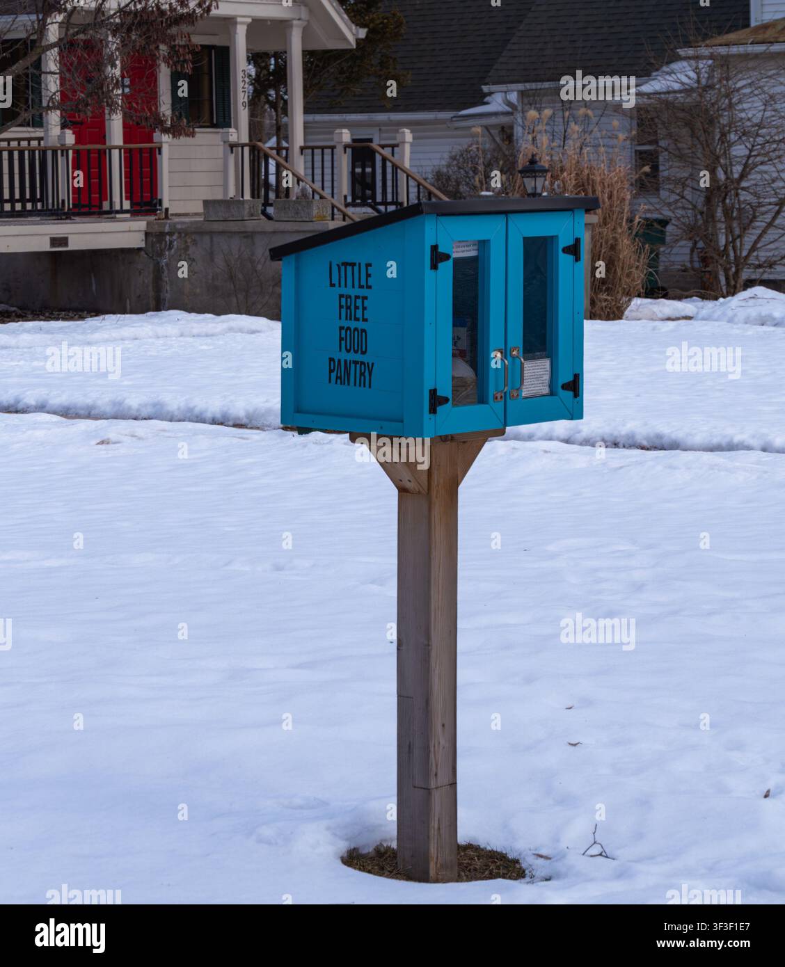 Helle blaue kleine Freigabeküche an einem Holzpfosten in einem verschneiten Nachbarschaftshof, die Gemeinschaftsunterstützung, Teilen, Wohltätigkeit und Winterhilfe für Bedürftige zeigt Stockfoto