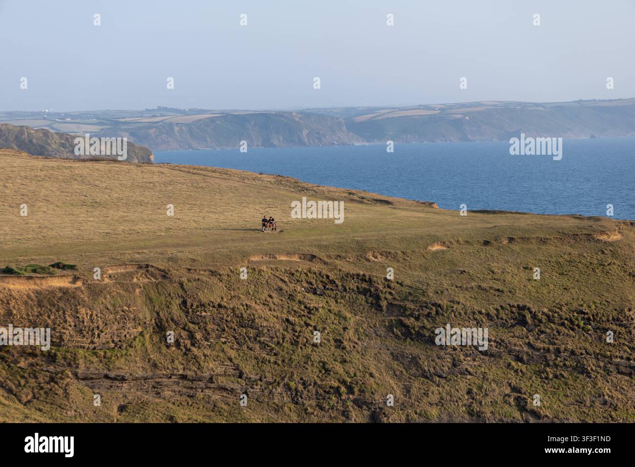Cornwall 2026 Bude, England - 18.7.2026: Zwei Männer sitzen auf einer Parkbank mit Blick auf die Klippen und Küstenpfade von Bude in Cornwall. England Stockfoto