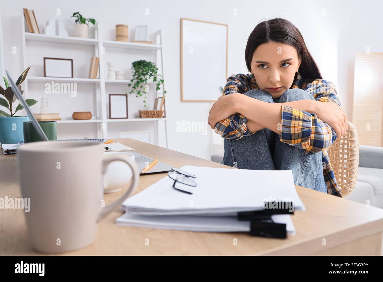 Junge Frau, die Stress und Angst verspürt, während sie von zu Hause aus arbeitet, sich an ihrem Schreibtisch überfordert und isoliert fühlt Stockfoto