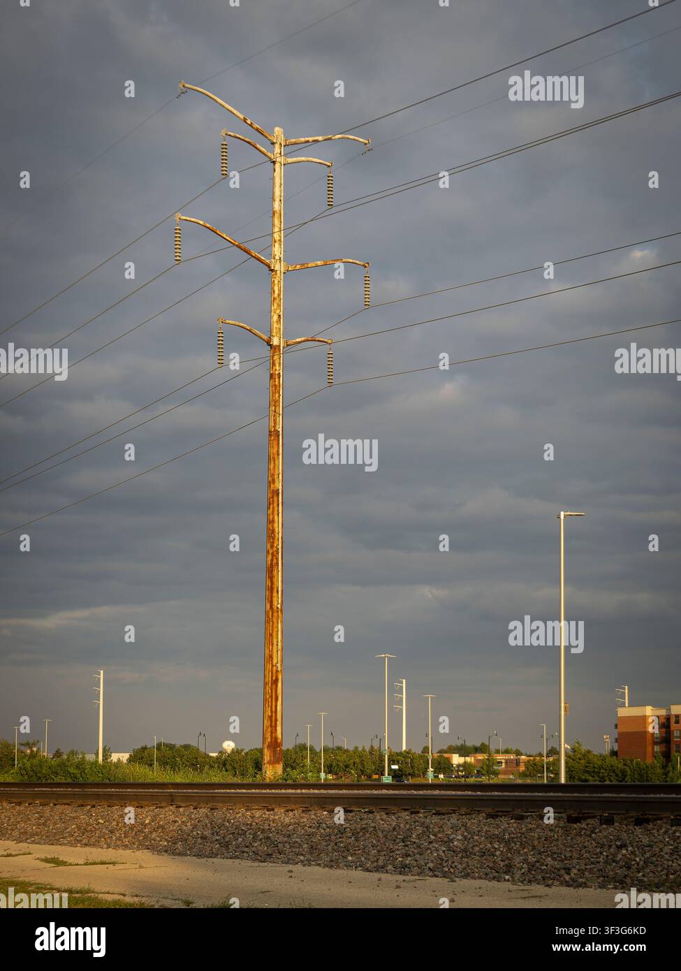 Ein hoher, verwitterter Holzstrommast steht neben Eisenbahngleisen unter einem dramatischen bewölkten Himmel in der Dämmerung Stockfoto
