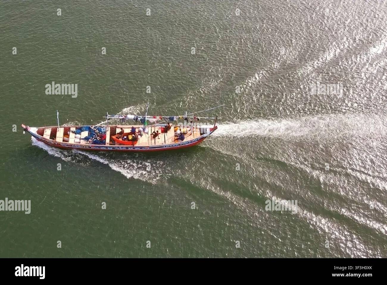 Luftbild eines traditionellen Holzfischerboots mit Menschen an Bord, das durch das Wasser fährt und einen weißen Kielwellenzug in Ghana erzeugt. Stockfoto