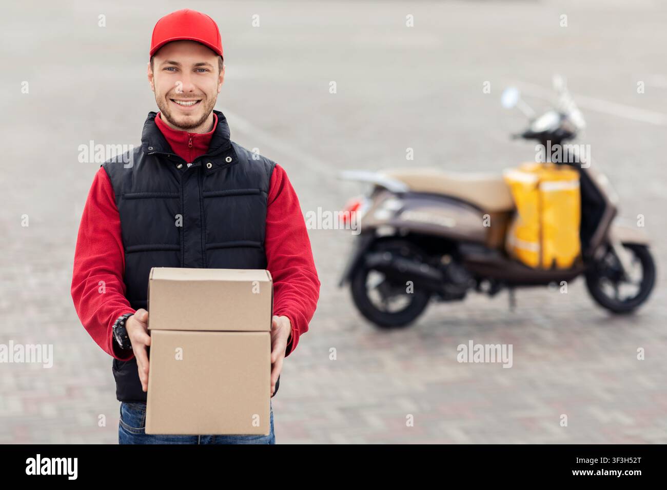 Fröhlicher Fahrer Hält Boxen Und Lächelnd In Der Nähe Des Motorrads In Der Stadt Stockfoto