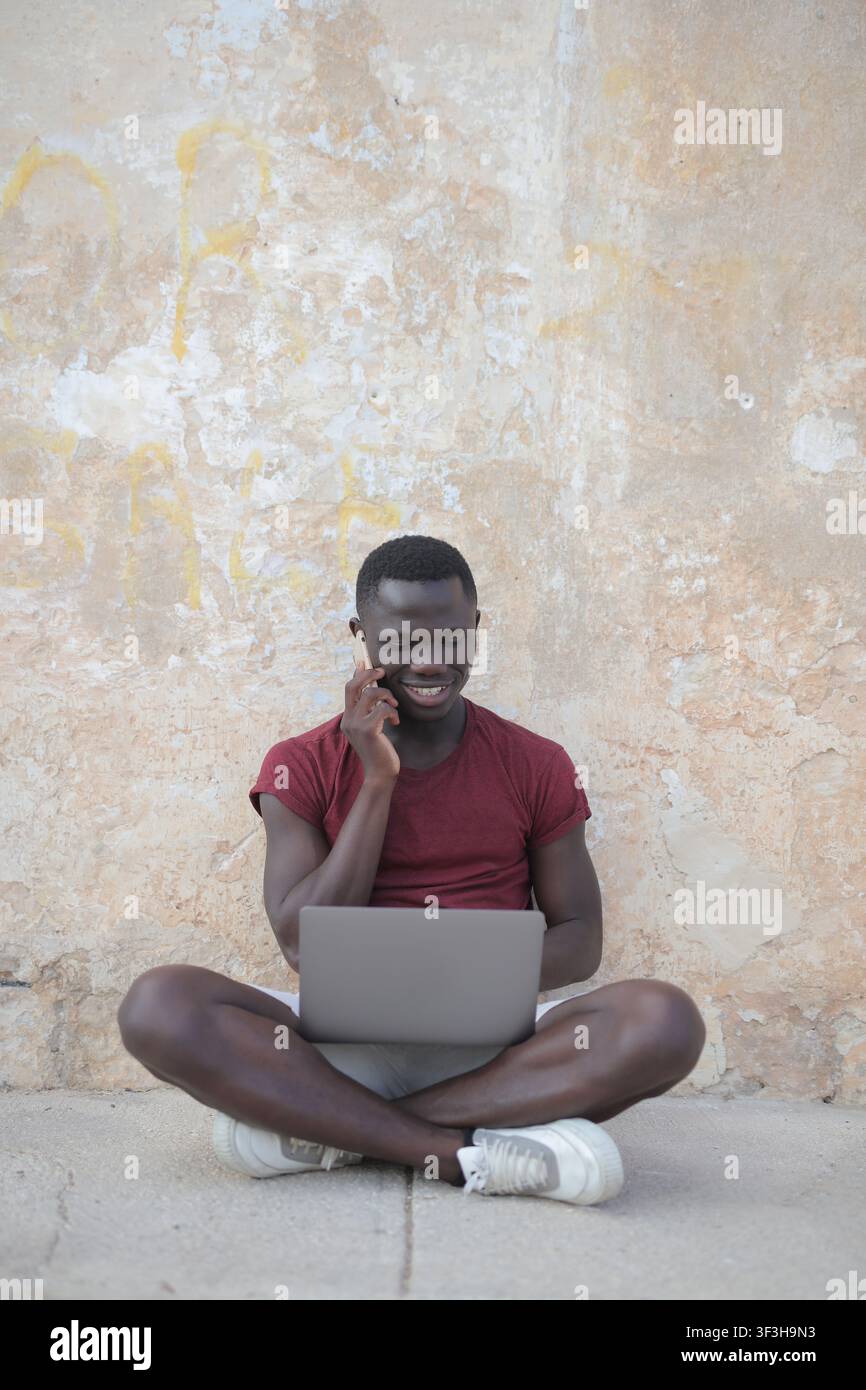 Junger Mann arbeitet remote mit Telefon und Laptop draußen Stockfoto