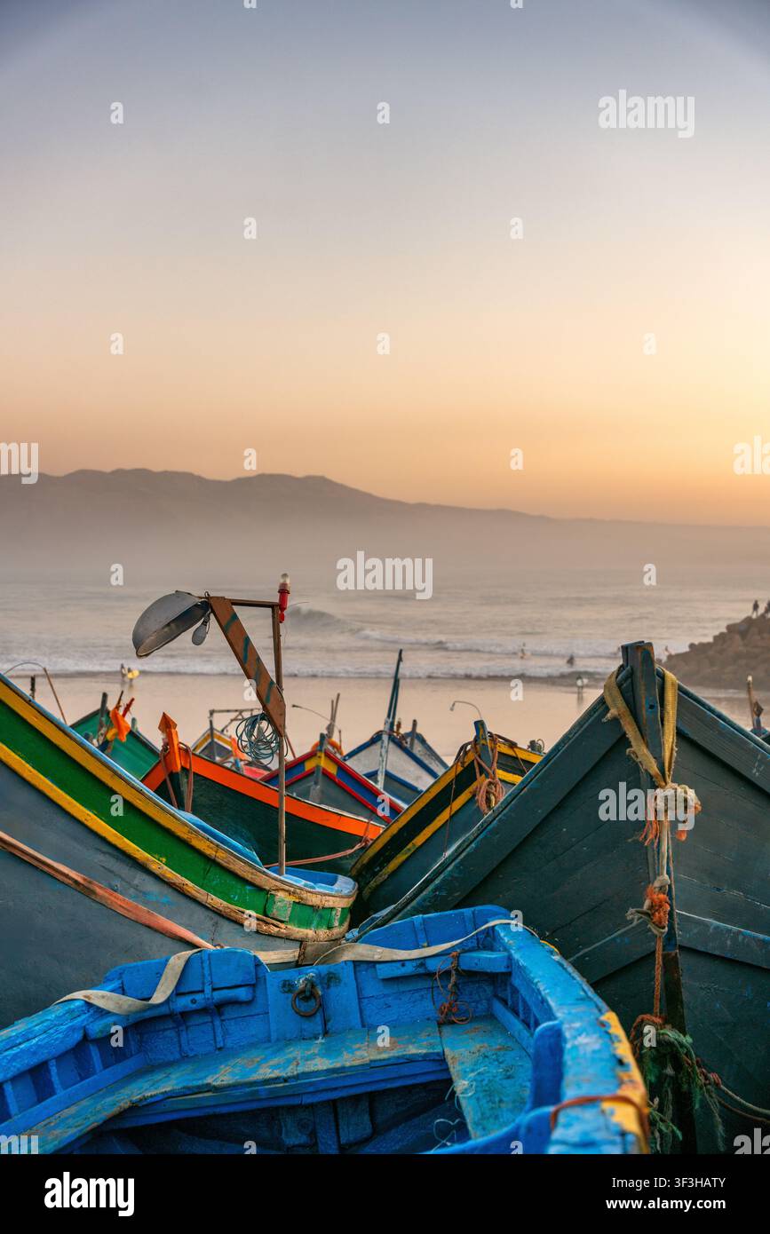 Farbenfrohe Fischerboote, die am Strand von Imsouane in Marokko bei Sonnenuntergang vertäut sind Stockfoto